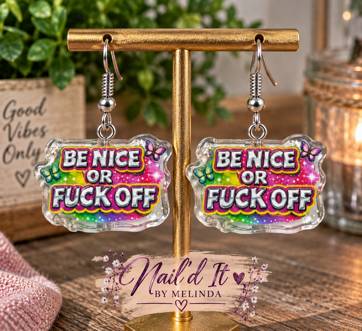 Be Nice or F*ck Off dangle earrings on gold display stand – Nail'd It By Melinda branded lifestyle shot