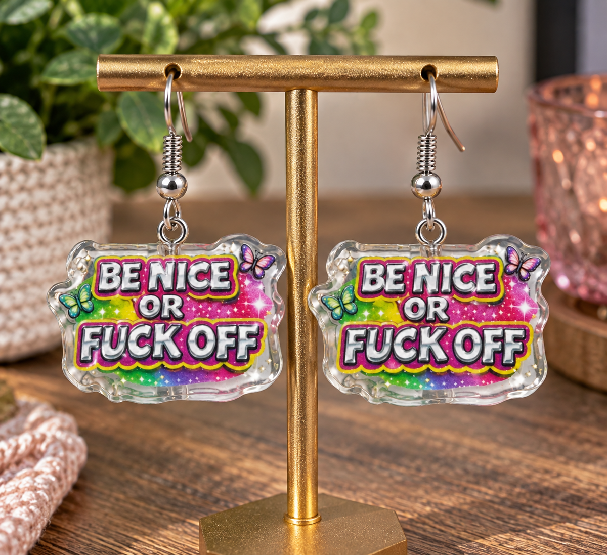 Be Nice or F*ck Off dangle earrings on gold display stand – lifestyle shot