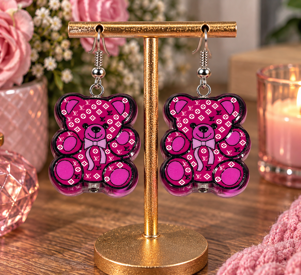 Pink teddy bear designer-inspired dangle earrings on gold display stand – lifestyle shot with pink florals