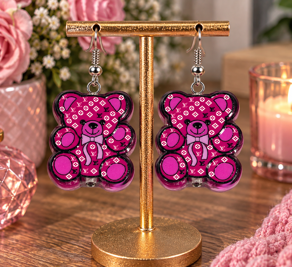Pink teddy bear designer-inspired dangle earrings on gold display stand – lifestyle shot with pink florals